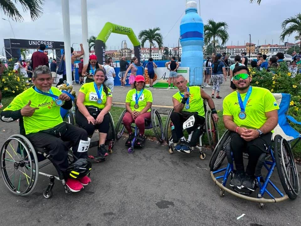 Cinco atletas en silla de ruedas con sus medallas junto al arco de meta