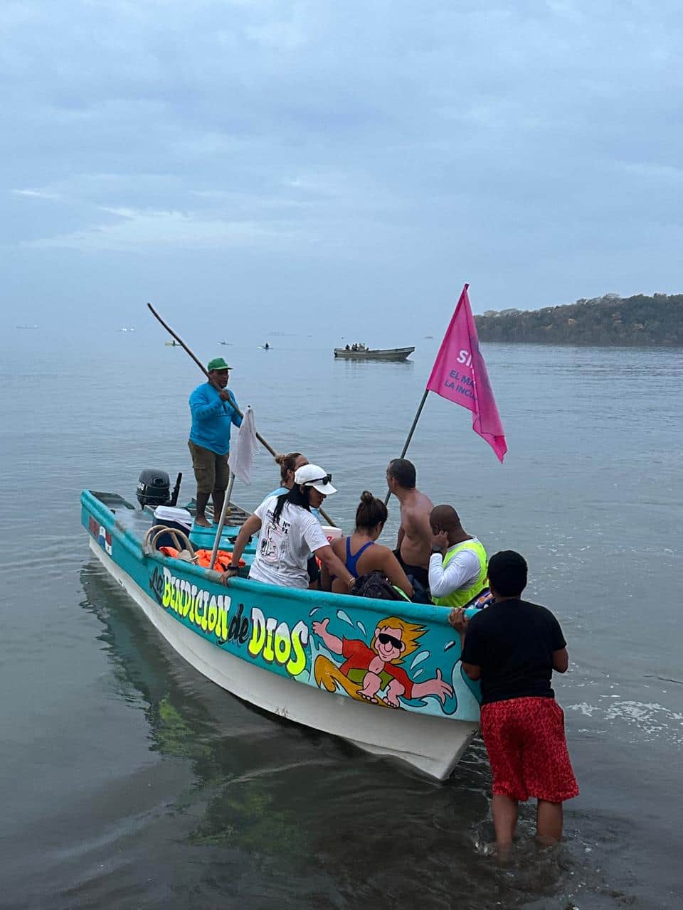 El bote de apoyo del cruce a nado, con su bandera rosada, junto a la orilla